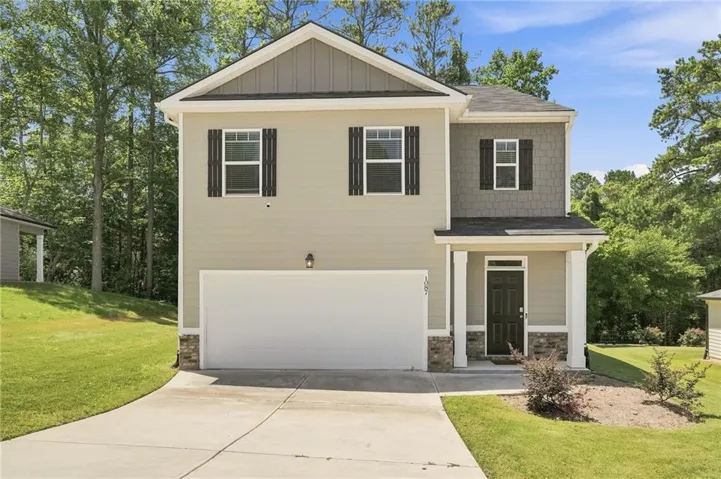Two-story residence featuring light beige siding with dark brown accents, a covered entry porch, an attached garage, a concrete driveway, and mature landscaping