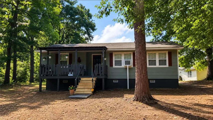 Single-story residence featuring a covered front porch, red window shutters, and mature trees