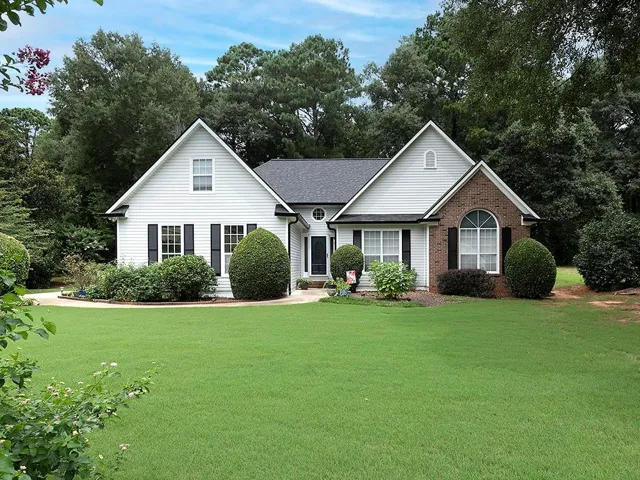 Exterior facade featuring white siding, brick accents, dark shutters, and a dark shingle roof