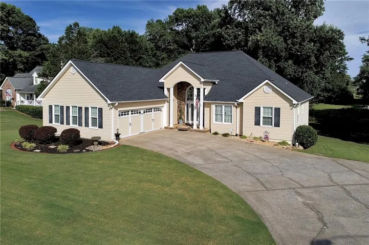 Cream-colored siding exterior featuring a three-car garage, black shutters, and an arched entry with columns