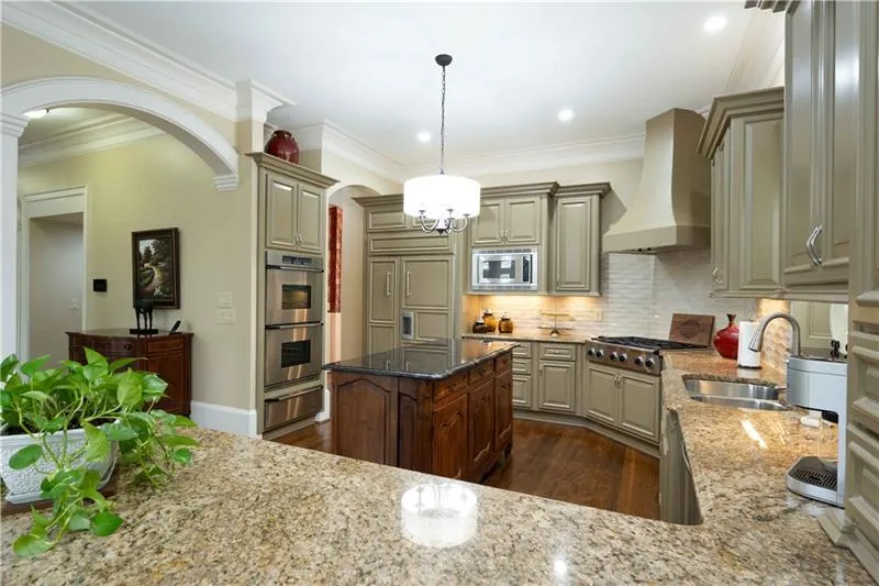 Kitchen with custom range hood, backsplash, light stone countertops, a kitchen island, and built in appliances