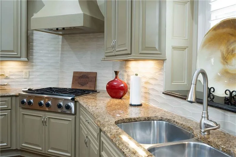Kitchen with light stone counters, tasteful backsplash, stainless steel gas cooktop, wall chimney exhaust hood, and sink