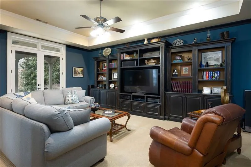 Living room with ceiling fan, a raised ceiling, light colored carpet, crown molding, and french doors