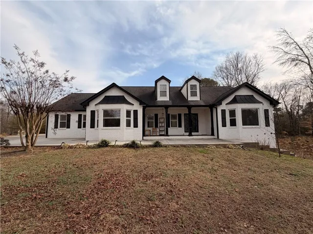 White brick exterior with black trim, multiple bay windows, and a covered front porch featuring decorative columns