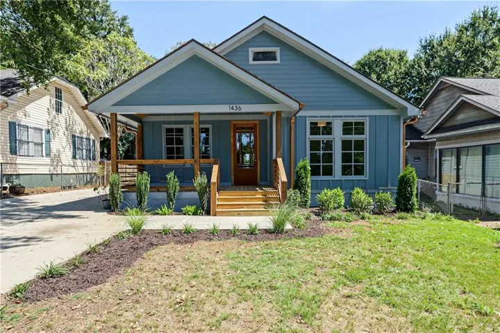 Light blue siding exterior with white trim, a covered front porch with natural wood pillars, a natural wood front door, and a landscaped front yard