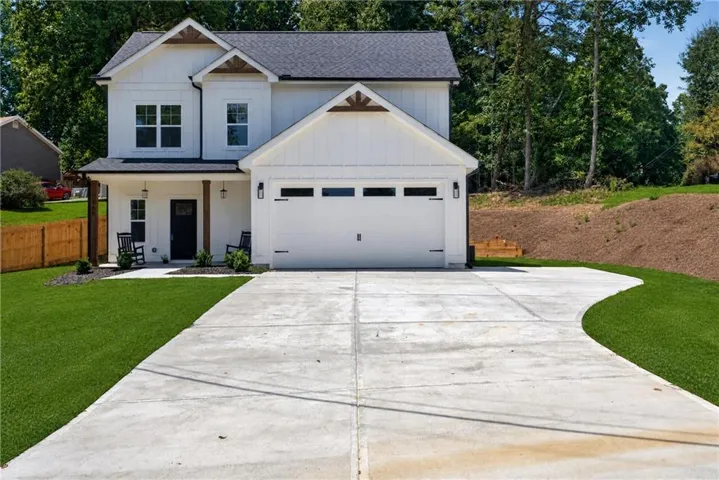 White vertical siding exterior with dark-framed windows, an attached garage, a covered front porch, and a concrete driveway