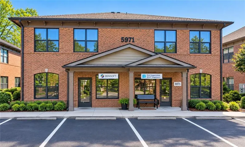 Brick facade building with a prominent covered entry, multiple large windows with dark framing, and integrated landscaping