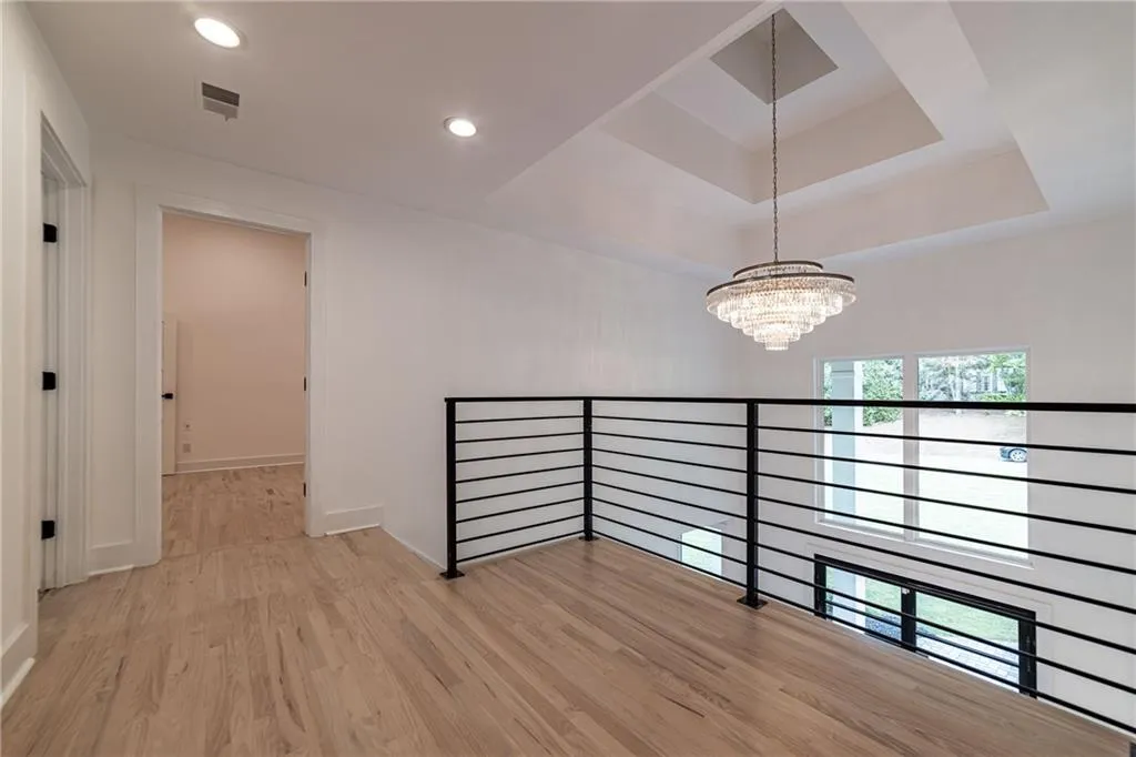Hall featuring wood finished floors, a chandelier, a raised ceiling, and recessed lighting
