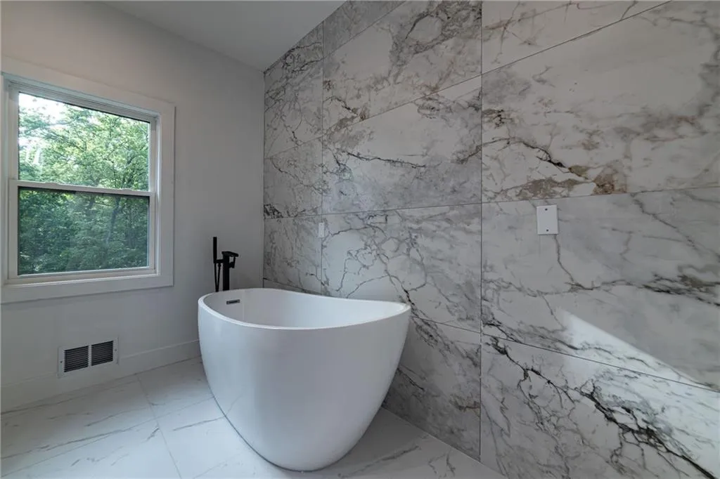 Bathroom featuring marble finish floors, a freestanding tub, and tile walls