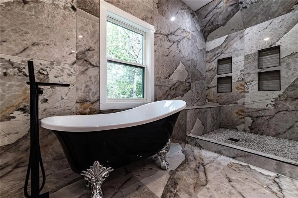 Bathroom with marble tiled floors, tile walls, a freestanding tub, and stone wall