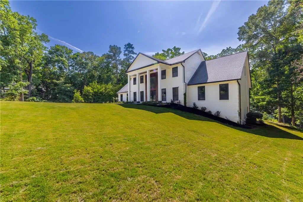 Greek revival inspired property featuring a front yard, brick siding, a shingled roof, and view of wooded area