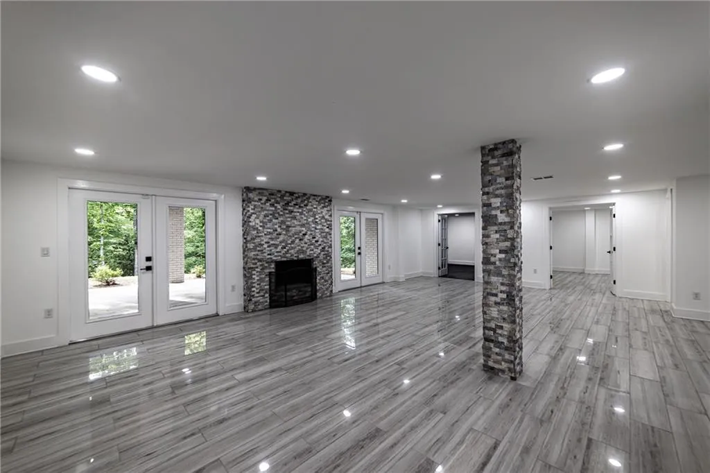 Unfurnished living room with french doors, recessed lighting, wood tiled floors, a stone fireplace, and decorative columns