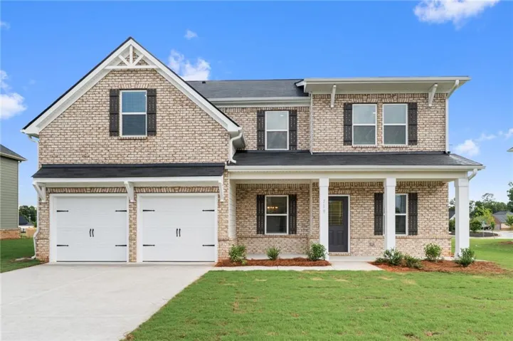 Two-story brick exterior featuring a covered front porch, a two-car garage with white doors, black shingled roof, and dark window shutters