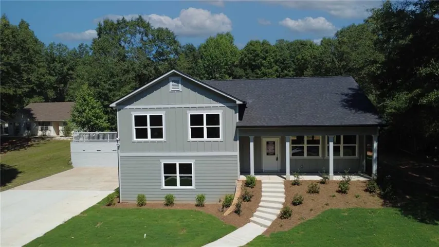 Modern two-story home featuring a light gray fiber cement exterior with contrasting dark roofing, paired double-hung windows with white trim, and a covered front porch with composite decking