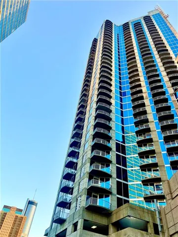 Modern condominium entrance featuring a prominent awning with branding, glass double doors, and architectural wall sconces