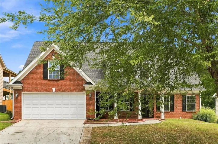 Brick facade residence featuring a front porch with white columns, a two-car garage, and a gabled roofline