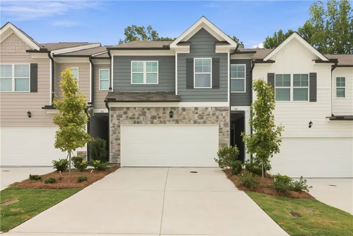 Contemporary townhome exterior featuring a stone and siding facade, white garage doors, and mature landscaping