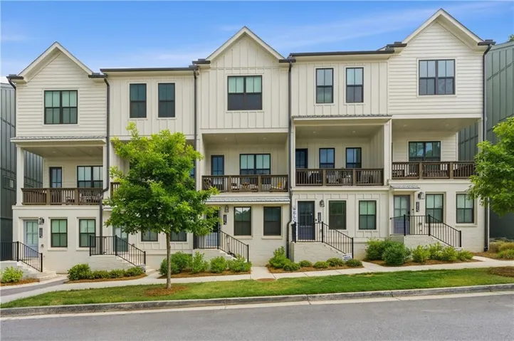 Modern townhome exterior featuring vertical and horizontal siding, multiple balconies with wood railings, and individual entry staircases with black metal handrails