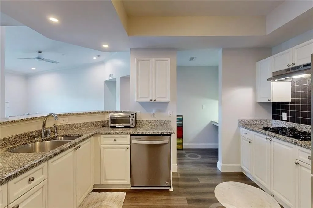 Kitchen featuring dishwasher, under cabinet range hood, black gas cooktop, light stone counters, and dark wood-style flooring
