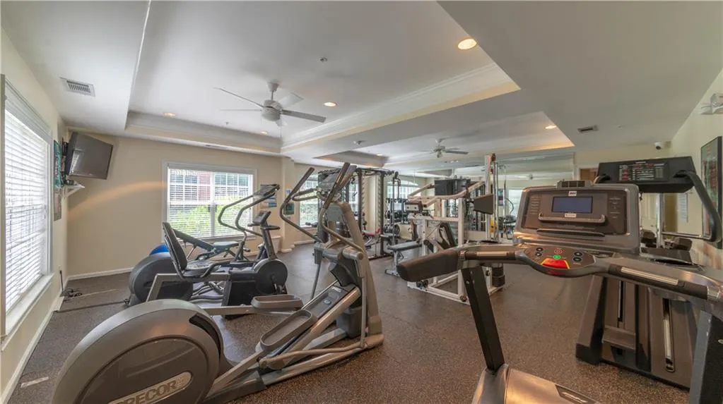 Workout area featuring ceiling fan, a raised ceiling, and ornamental molding