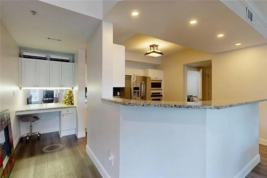 Kitchen with stainless steel appliances, dark wood-style flooring, built in study area, white cabinets, and recessed lighting