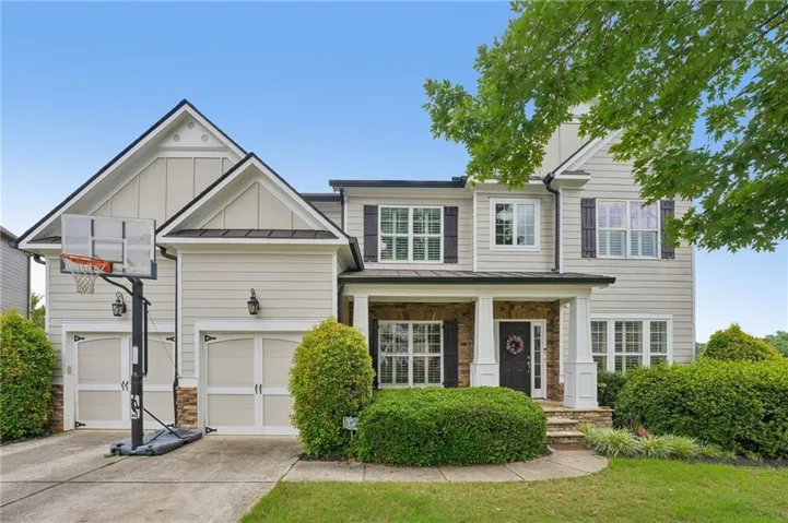 Two-story home featuring a combination of siding and stone veneer, a covered porch with white columns, and a two-car garage