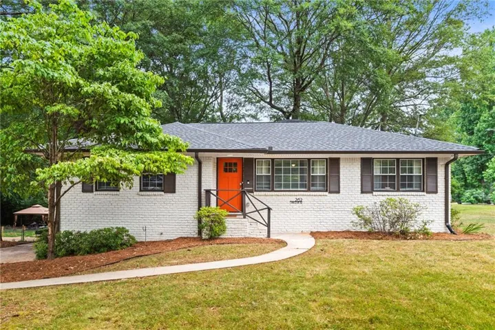 White painted brick exterior with dark shutters, an orange front door, a dark gray roof, and a curved concrete walkway