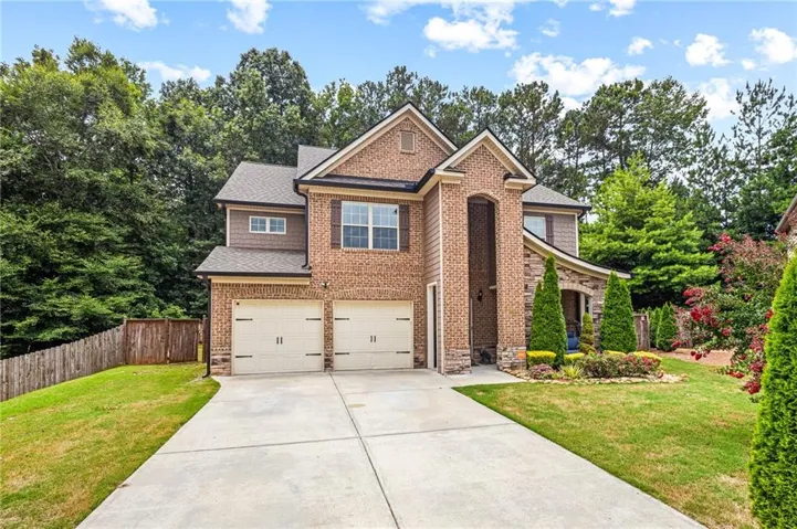 Brick and stone facade residence featuring a two-car garage, mature landscaping, and a concrete driveway