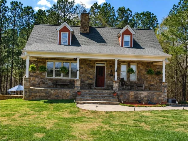 Stone veneer exterior featuring a covered front porch with white columns, a dark red front door, and two dormer windows