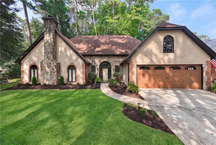 Stone and stucco exterior featuring a prominent stone chimney, arched windows, and a wood-finish garage door