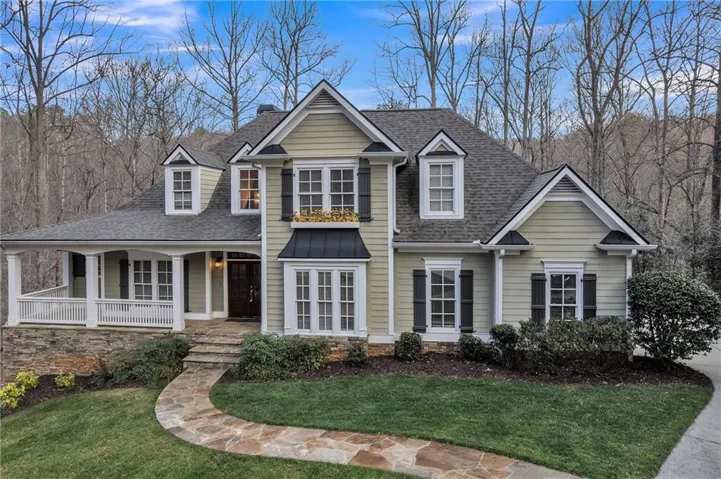 Traditional two-story residence featuring dormer windows, a covered front porch with white railings, and a stone-clad foundation