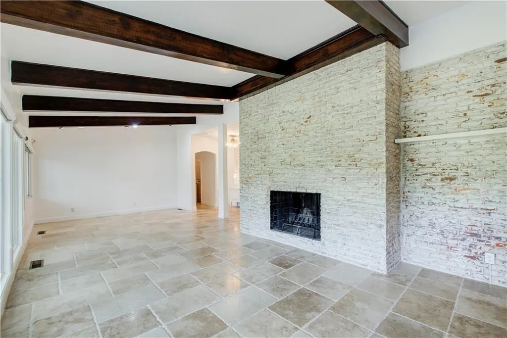 Unfurnished living room featuring stone tile flooring, beamed ceiling, arched walkways, a fireplace, and baseboards