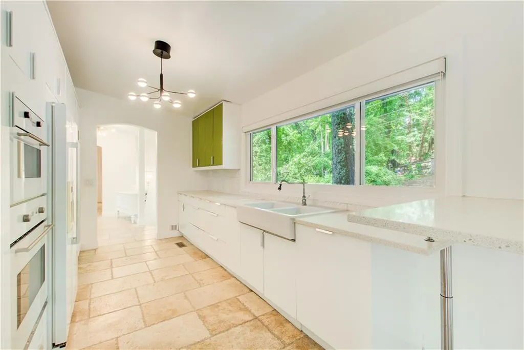 Kitchen with a sink, arched walkways, white double oven, stone tile flooring, and white cabinets