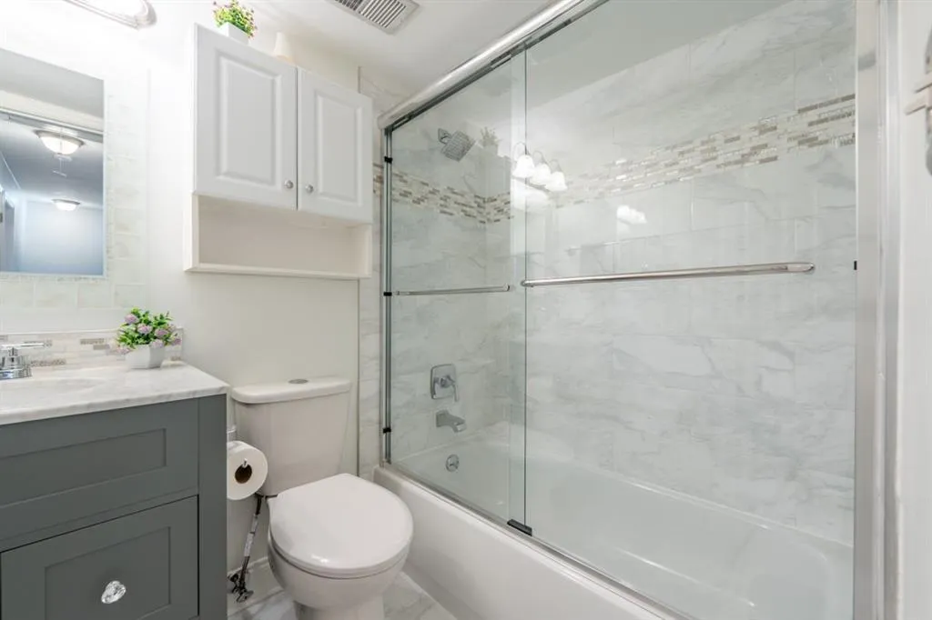 Guest Bathroom featuring toilet, visible vents, vanity, combined bath / shower with glass door, and backsplash