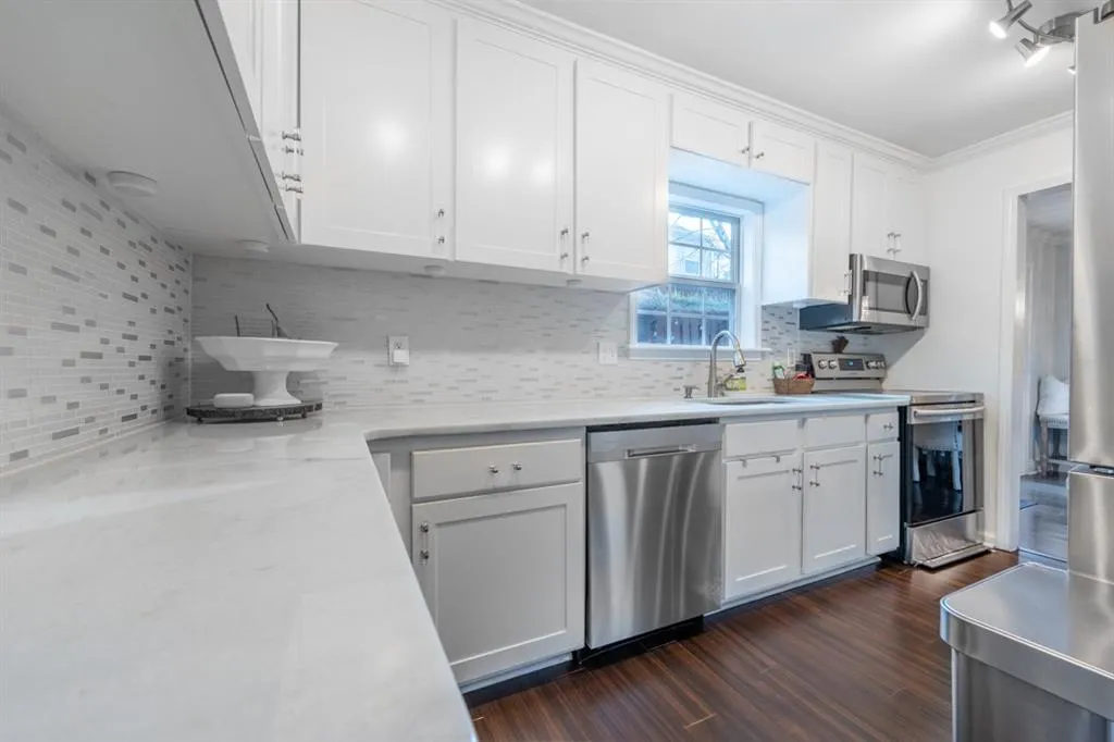 Kitchen featuring dark wood-type flooring, a sink, white cabinets, appliances with stainless steel finishes, and tasteful backsplash