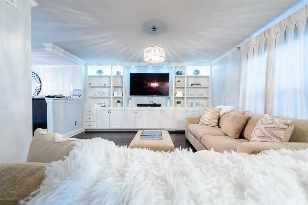 Living room featuring an inviting chandelier, crown molding, built in shelves, and dark wood-style flooring