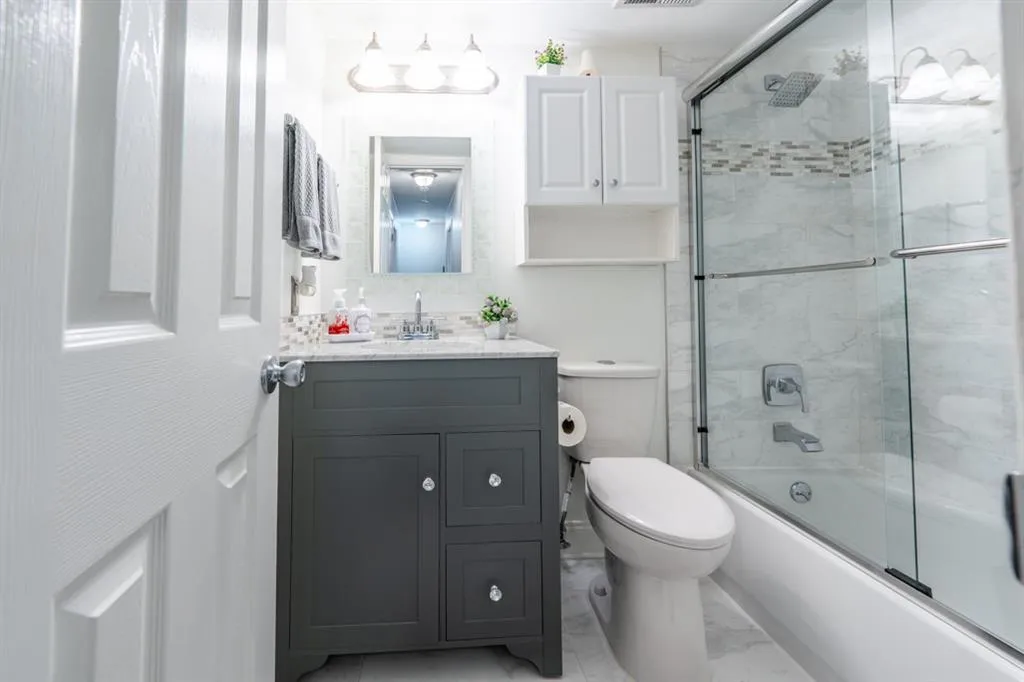 Guest Bathroom/ Hallway Bathroom featuring marble finish floor, visible vents, toilet, combined bath / shower with glass door, and vanity
