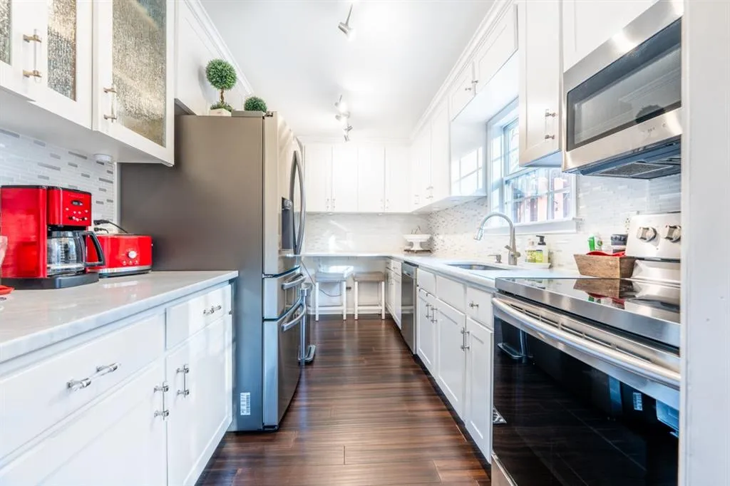 Kitchen featuring dark wood finished floors, white cabinets, glass insert cabinets, appliances with stainless steel finishes, and a sink