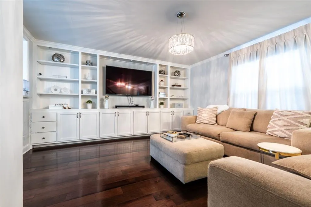 Living area featuring a chandelier, dark wood-style flooring, ornamental molding, and built in features