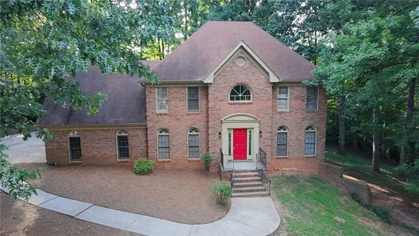 Striking brick Colonial elevation featuring a symmetrical facade with arched entry portico, red lacquered front door, multi-pane windows with dark shutters, and a prominent peaked roof with dormers