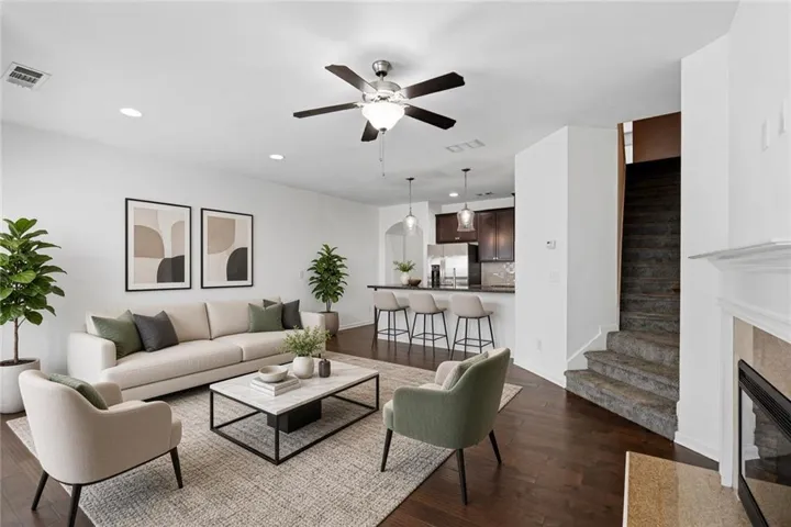 Virtually Staged - Spacious living area featuring dark wood-finish flooring, a ceiling fan with integrated lighting, recessed lighting, and a fireplace with a mantel