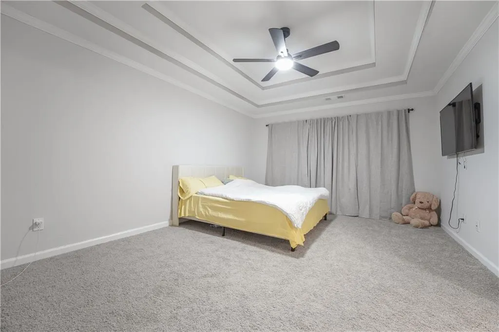 Carpeted bedroom featuring a raised ceiling, ceiling fan, and crown molding