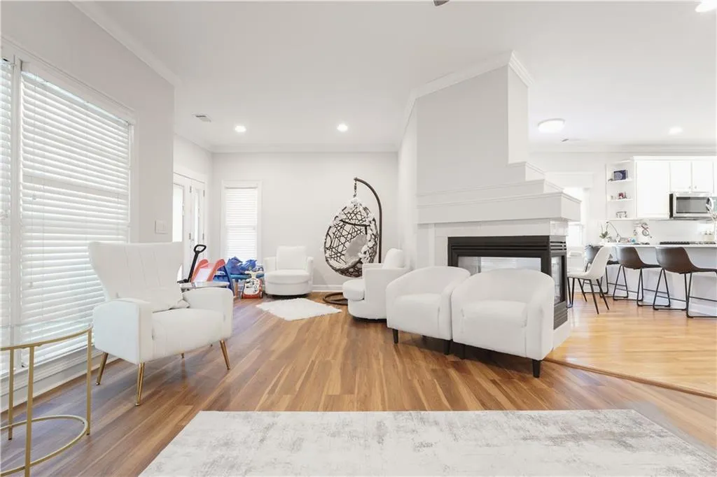 Living area with ornamental molding, light wood-type flooring, a multi sided fireplace, and recessed lighting