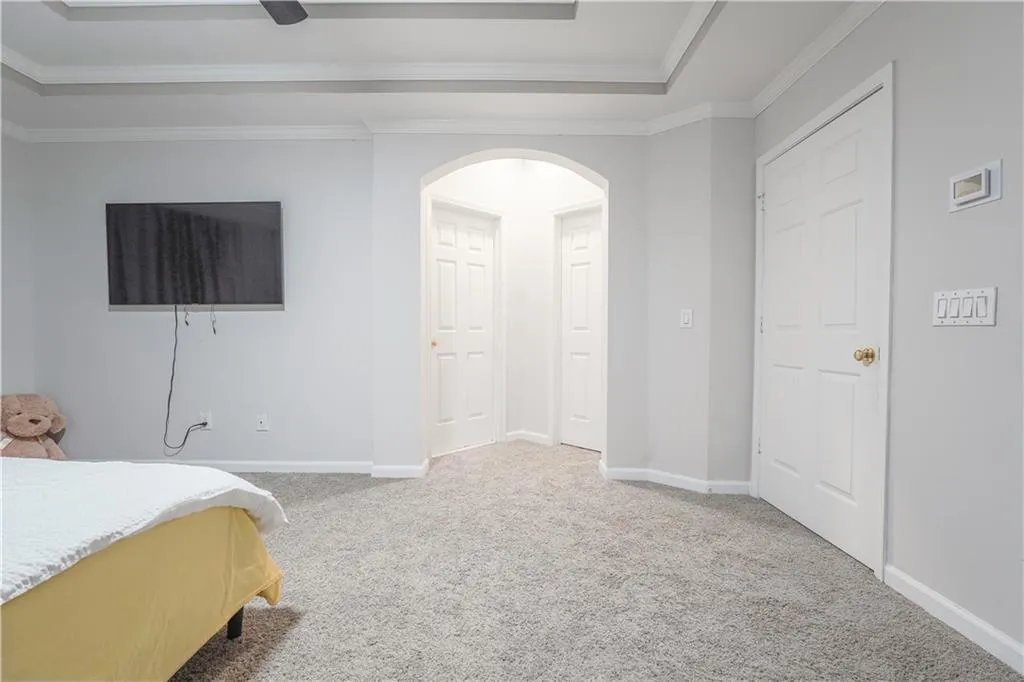 Bedroom featuring light colored carpet, a raised ceiling, a ceiling fan, ornamental molding, and arched walkways