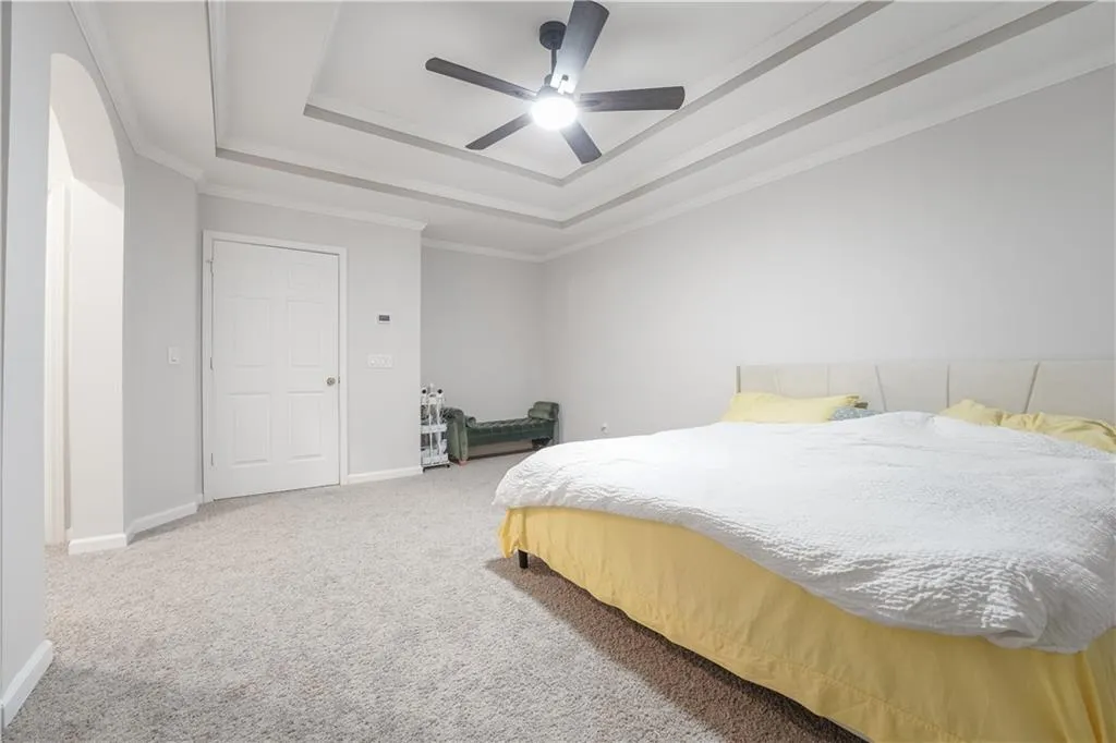 Bedroom with a tray ceiling, light carpet, a ceiling fan, and crown molding