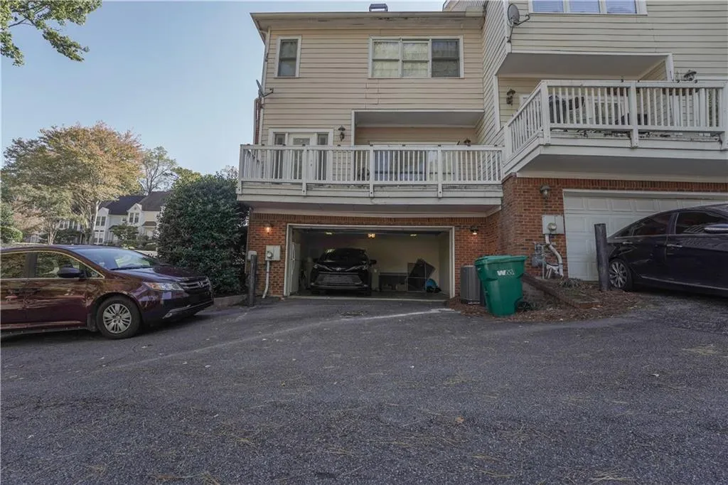 Back of property featuring brick siding, a balcony, driveway, and an attached garage