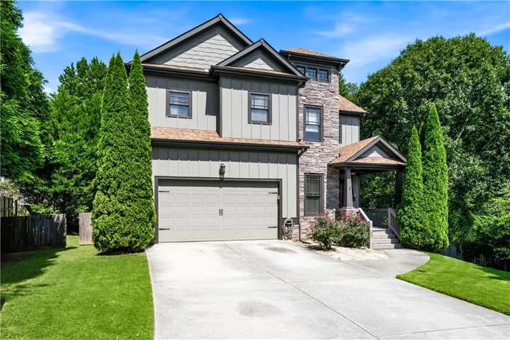 Stone and siding exterior with a covered entry, two-car garage, and mature landscaping