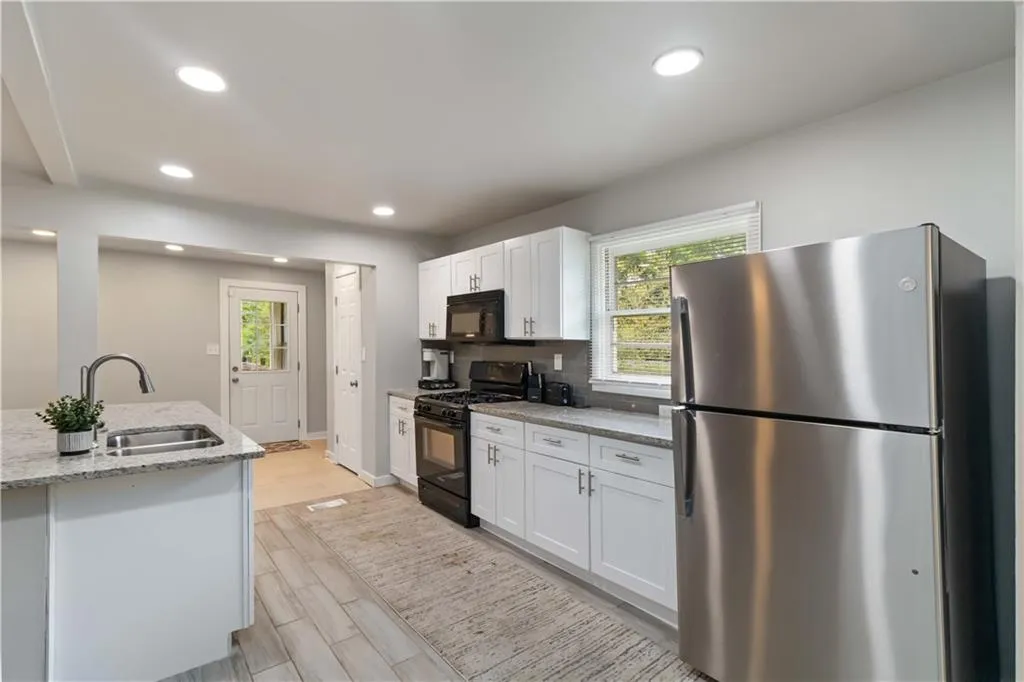 Kitchen with black appliances, white cabinets, recessed lighting, light stone countertops, and light wood-type flooring