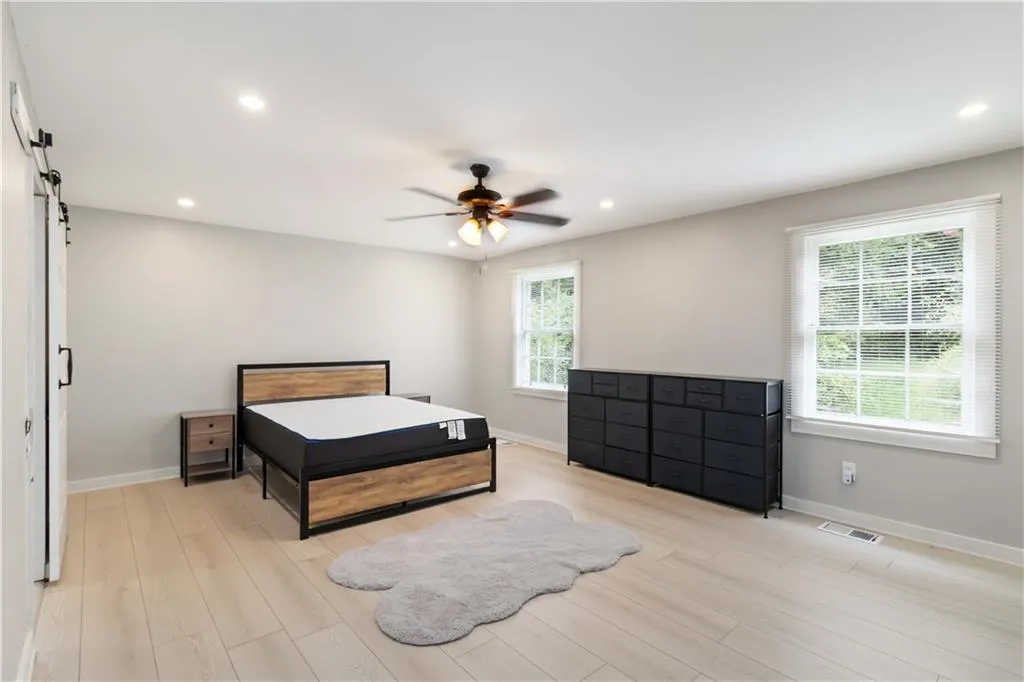 Bedroom with a barn door, light wood-style floors, a ceiling fan, and recessed lighting