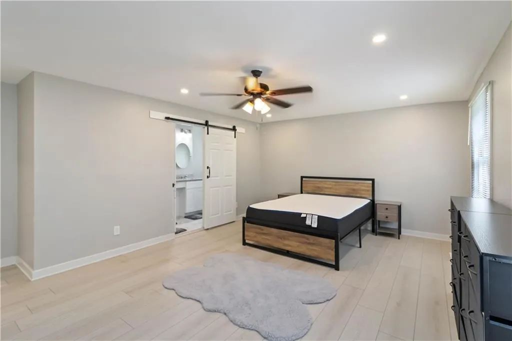Bedroom featuring a barn door, light wood finished floors, recessed lighting, ceiling fan, and ensuite bath